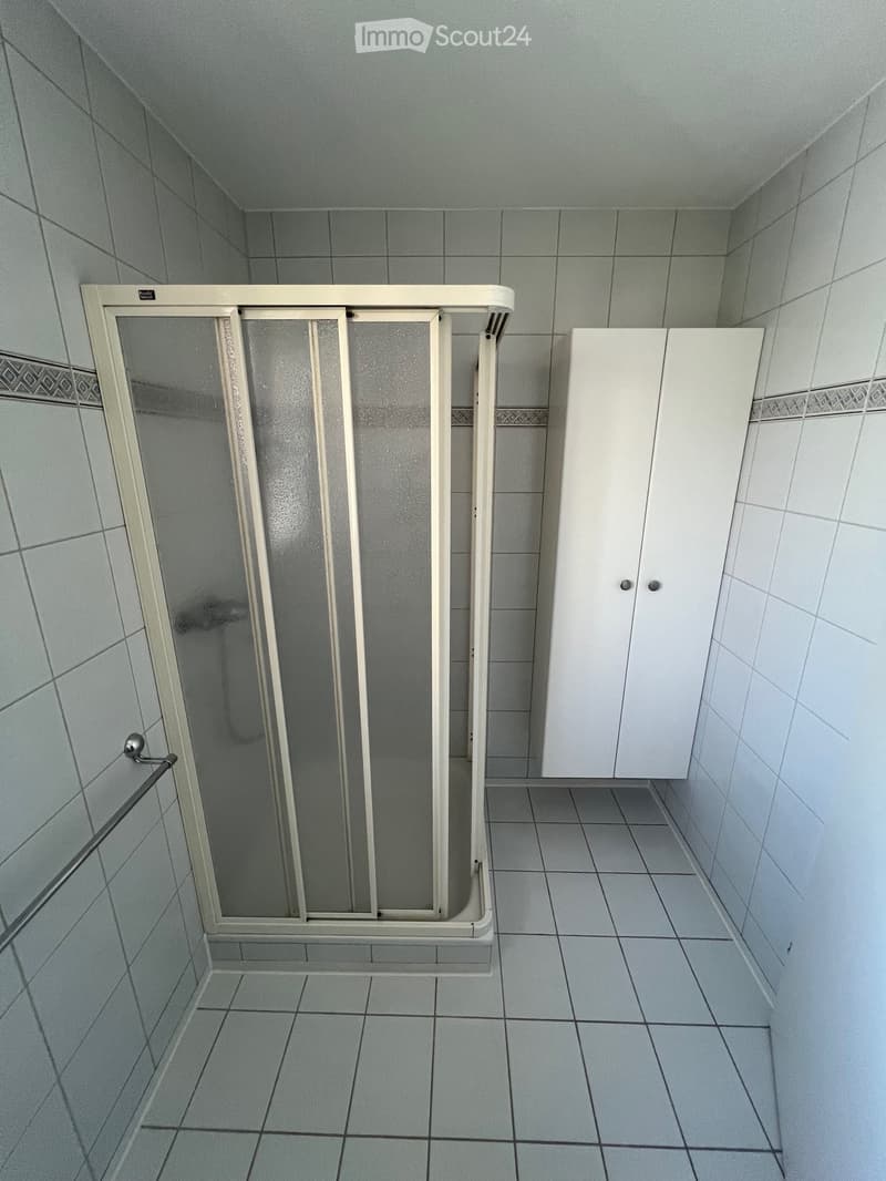 Bathroom with tiled walls and floor, a white cabinet, and a shower stall with a glass door.