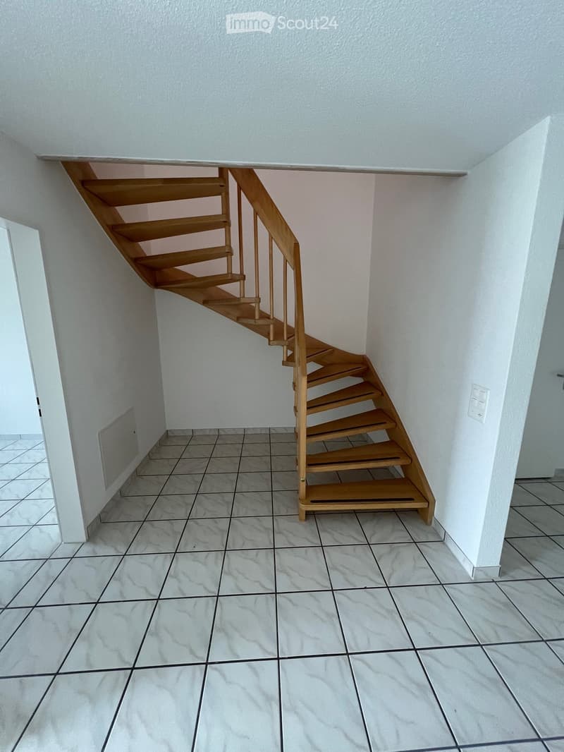 Empty hallway with tiled floor and white walls, featuring a wooden spiral staircase leading upwards.