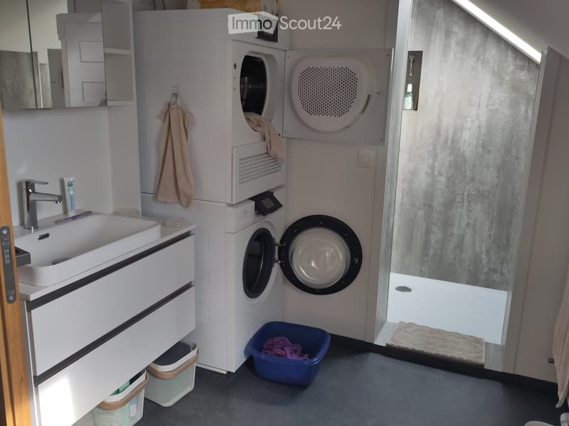 Modern bathroom with a white sink, faucet, washing machine, dryer, mirror, and a towel hanging on the wall.