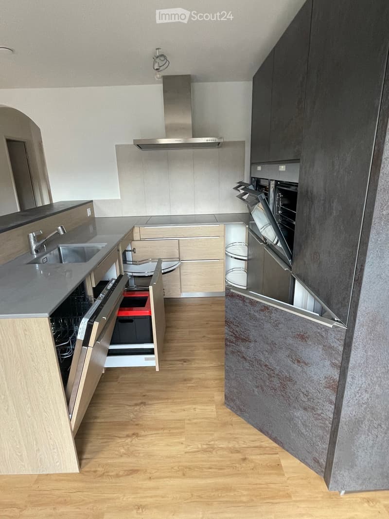 Modern kitchen with light wooden flooring, grey countertops, stainless steel appliances, and dark grey cabinets.