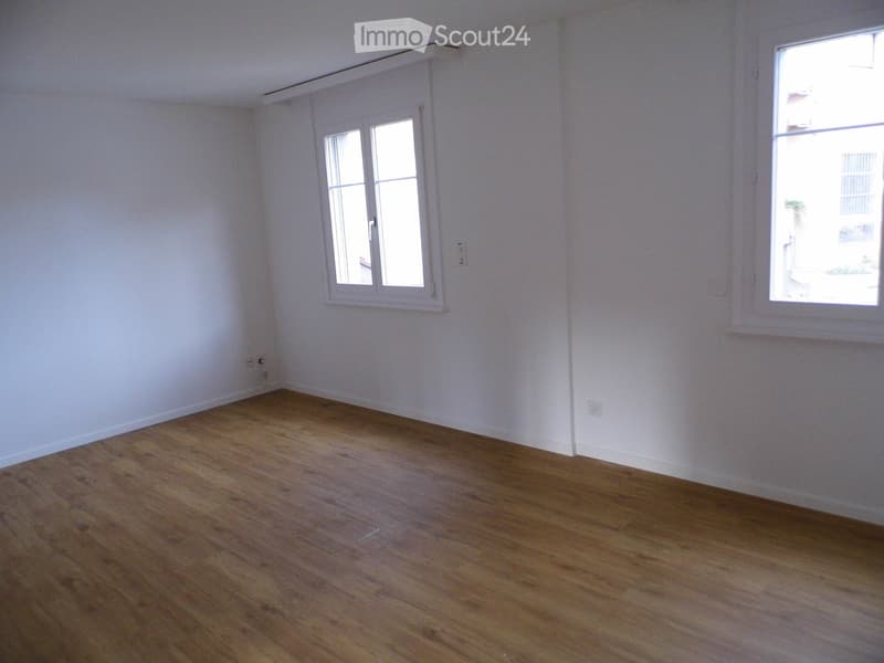 Empty room with wooden flooring and white walls, featuring two windows with white frames and visible electrical outlets.