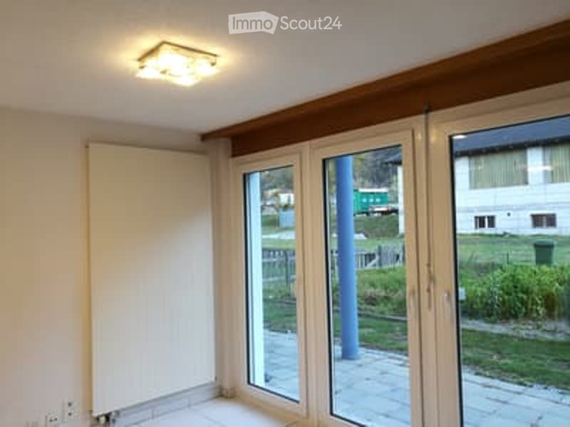 Empty room with large windows and sliding doors leading to a balcony, white walls, and a radiator.