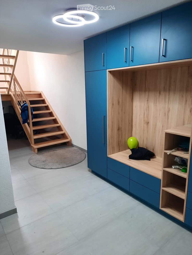 Modern hallway with blue and wooden built-in storage units, a round rug, and a staircase leading upwards.