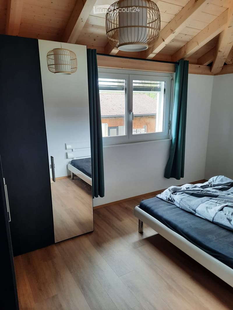 Cozy attic bedroom with wooden floors, two beds, large windows with curtains, and modern pendant lights.