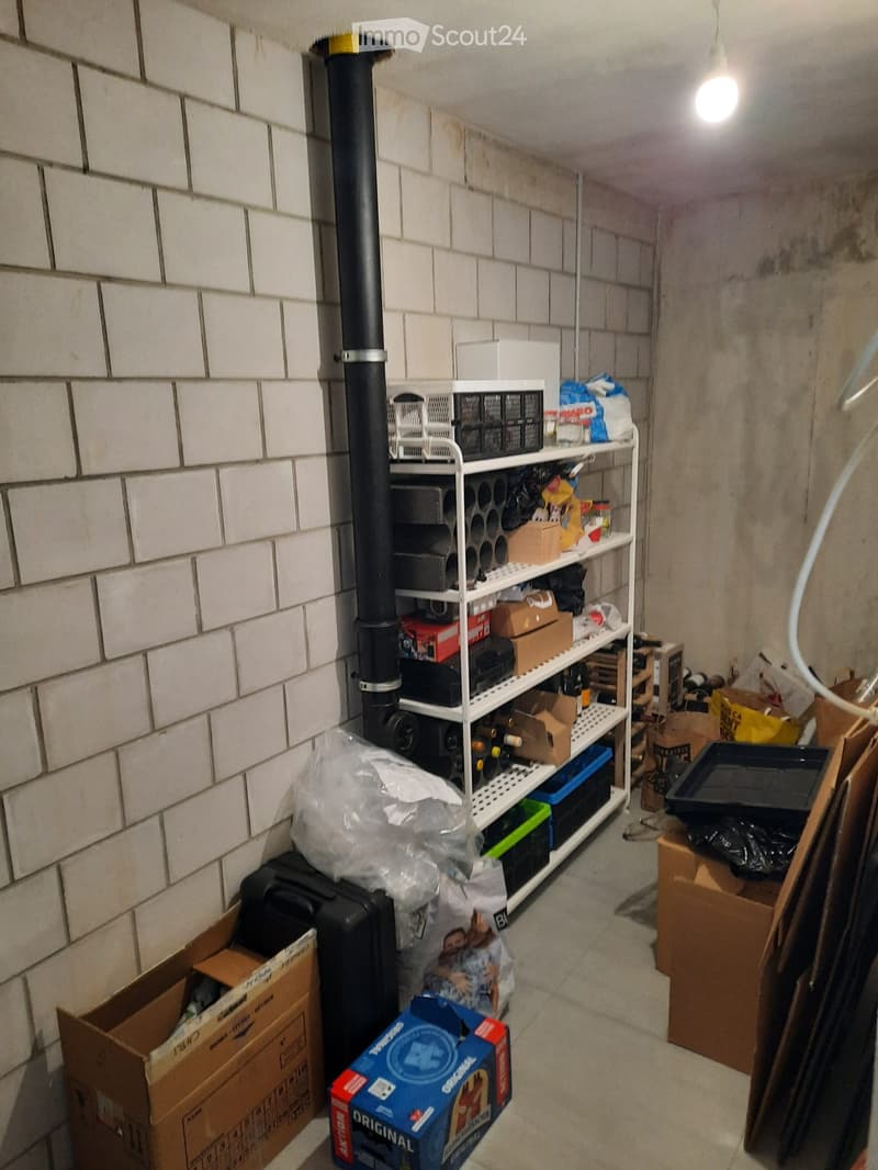 Storage area with white brick walls, metal shelving unit filled with boxes, tools, and miscellaneous items, along with plastic bags and cardboard boxes on the floor.