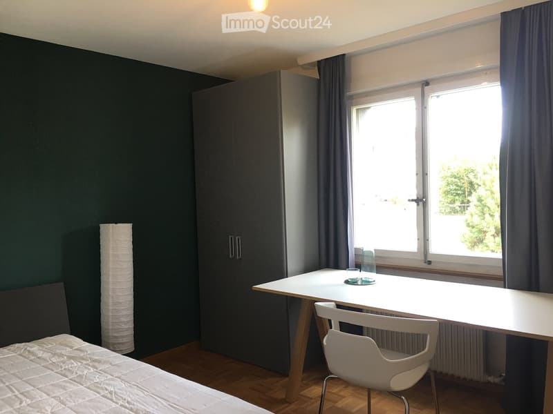 Modern bedroom with a bed, white table, chair, wardrobe, and a lamp near the window.