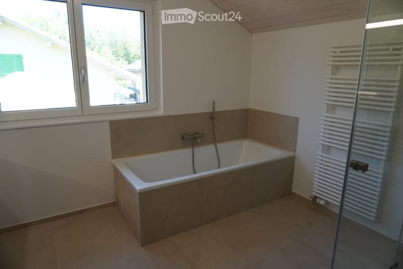 Bathroom with a bathtub, tiled walls, a radiator, and a window offering a view of the outside.