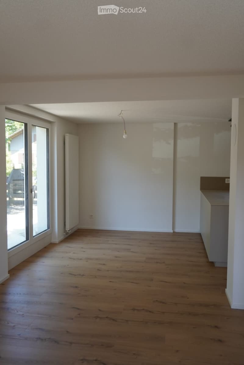 Empty room with wooden flooring, white walls, large windows, and a radiator. No furniture or equipment present.