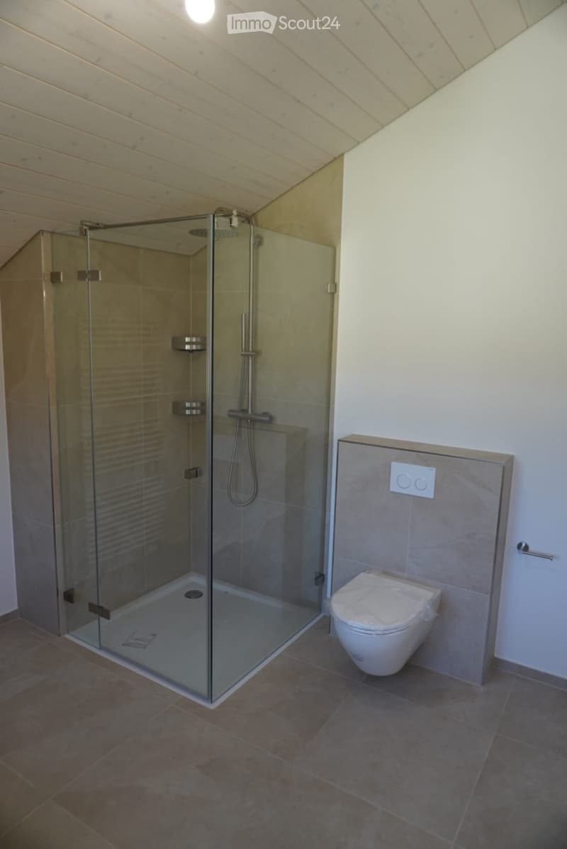 Modern bathroom with a glass-enclosed shower and a toilet, featuring wooden slatted ceilings and tiled floors.
