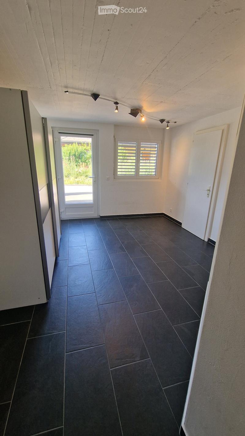 Empty room with dark tiled floor, white walls, and a door leading outside. No furniture or equipment visible.