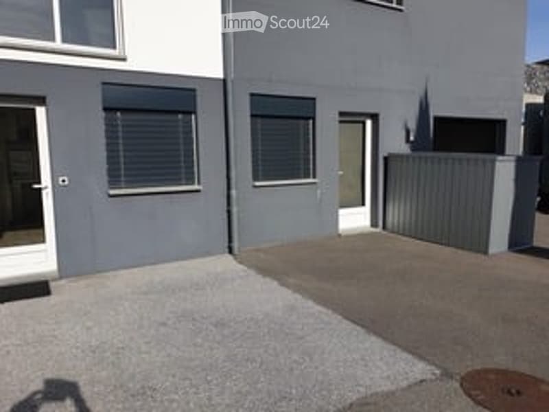 Modern two-story building with grey facade, white trim, and a small paved entrance area.