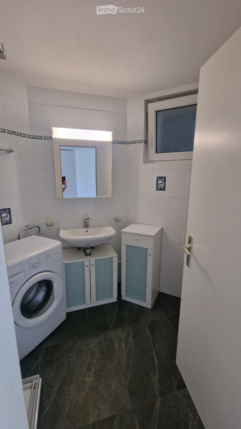 Bathroom with a sink, mirror, washing machine, and cabinets.