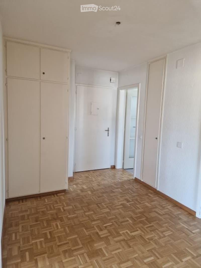 Empty hallway with wooden flooring, white walls, and built-in storage units on one side. A closed door leads to another room.