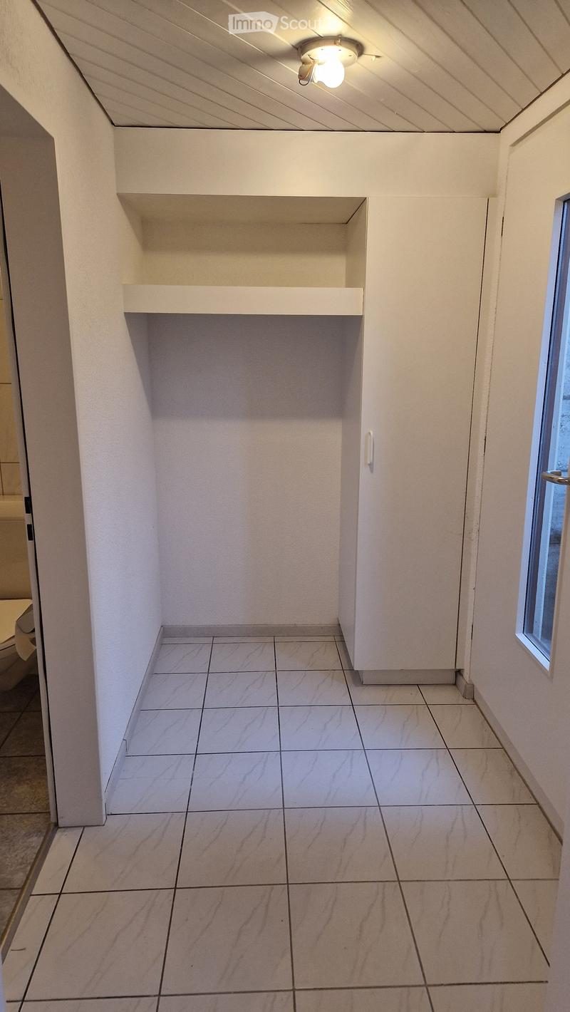 Empty hallway with white tiled floor, white walls, built-in shelving unit, and a small window on the right side.