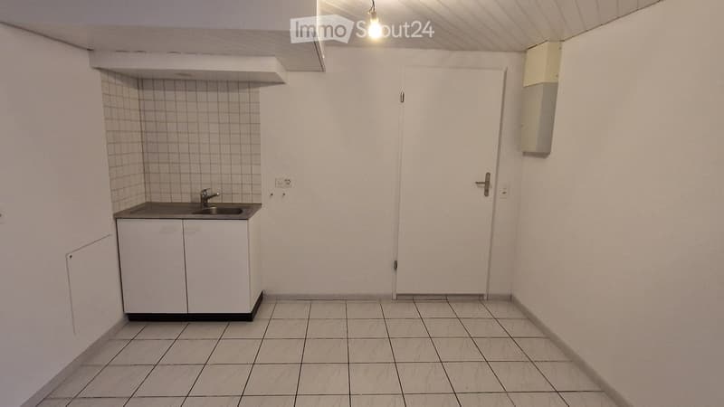 Empty room with tiled floor, white walls, a small sink with cabinet, and a closed door.