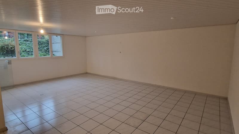 Empty room with tiled floor, light-colored walls, and four windows showing greenery outside.