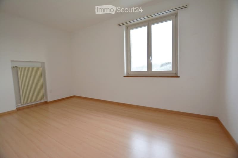 Empty room with light wooden flooring, white walls, a single window, and a radiator on one wall.