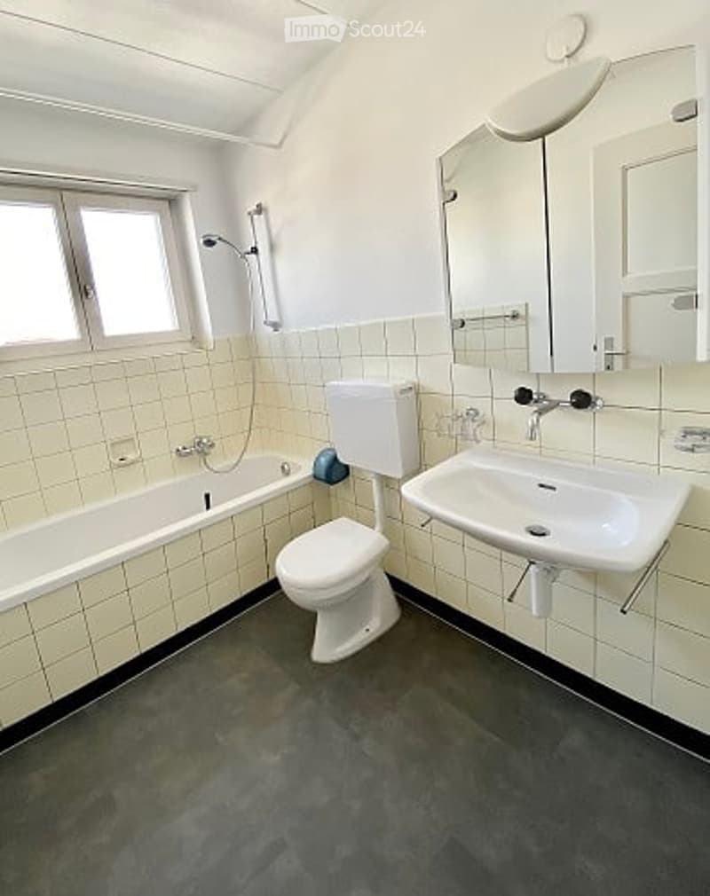 Bathroom with a bathtub, toilet, sink, mirror, and tiled walls.
