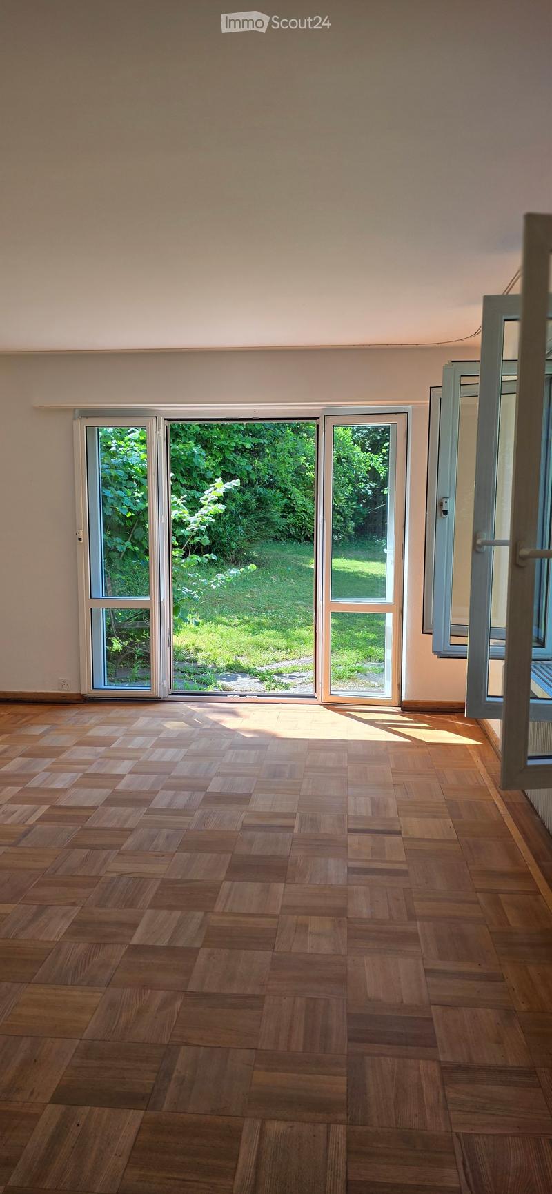 Empty room with wooden flooring and large sliding glass doors leading to a green outdoor area.
