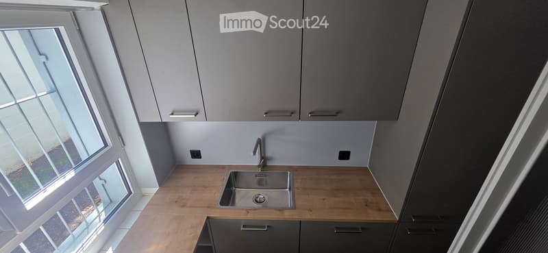 Modern kitchen with wooden countertop, stainless steel sink, and grey cabinets.