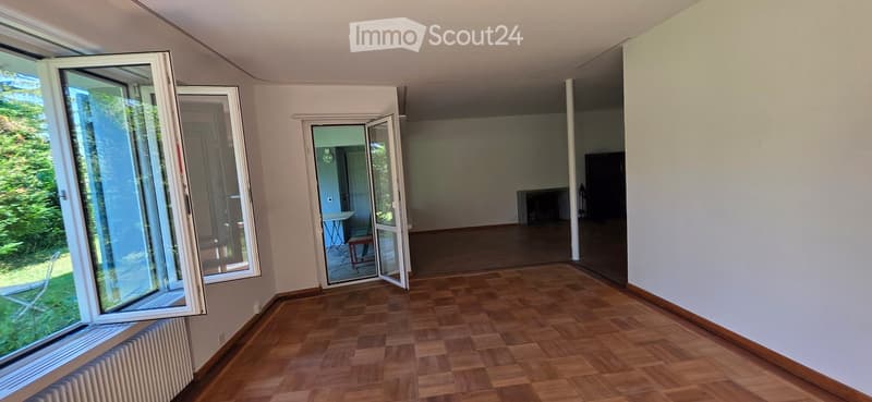 Empty room with wooden flooring, large windows, and an open doorway leading to another space.