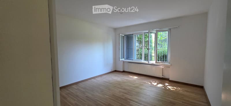 Empty room with wooden flooring, white walls, and large windows with open shutters, allowing natural light to fill the space.