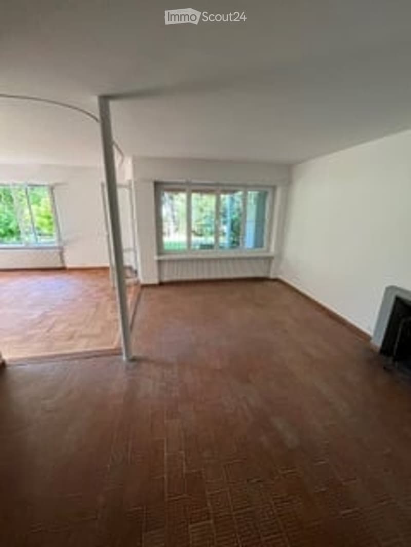 Empty room with wooden flooring, white walls, large windows, and radiator. No furniture or equipment present.