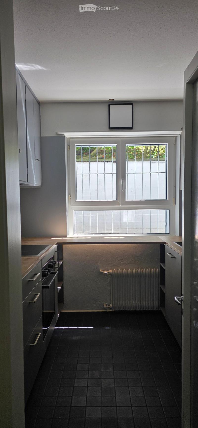 Modern kitchen with dark tiled floor, grey cabinets, a stove, and a radiator under a large window with bars.