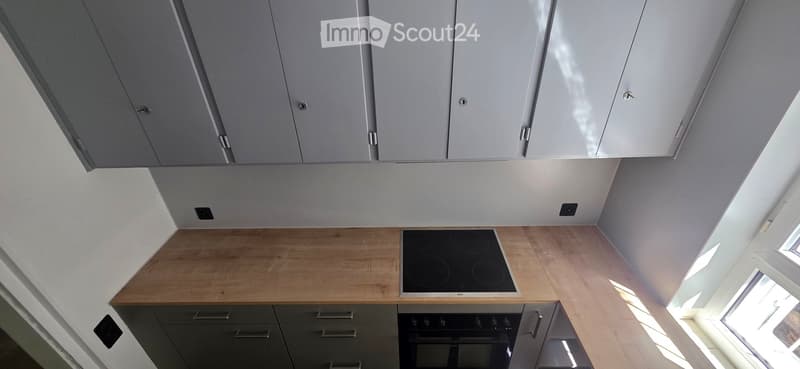 Modern kitchen with light grey cabinets, wooden countertops, and built-in appliances including an induction cooktop and oven.