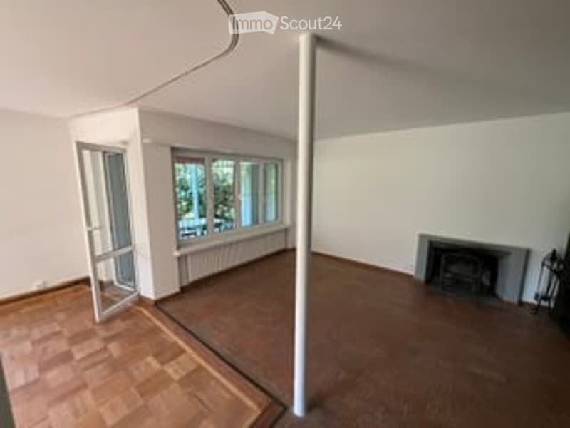 Empty room with wooden flooring, white walls, large windows, fireplace, and a white column. No furniture or equipment present.