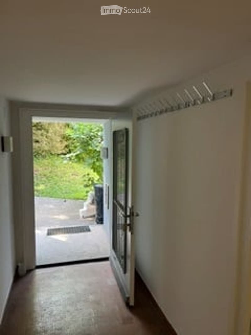 Empty hallway with wooden flooring, white walls, and an open door leading to a garden area.