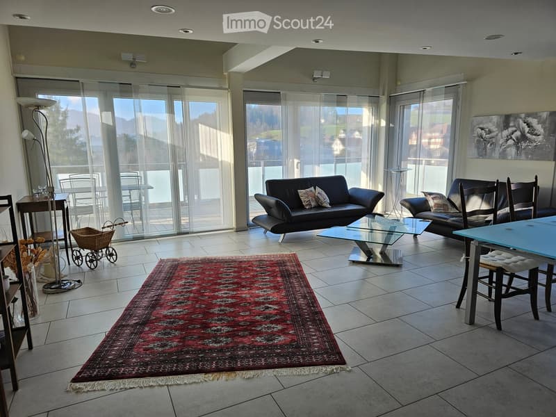 Large glass windows, couch with pillows, table, rug, chairs, blue desk