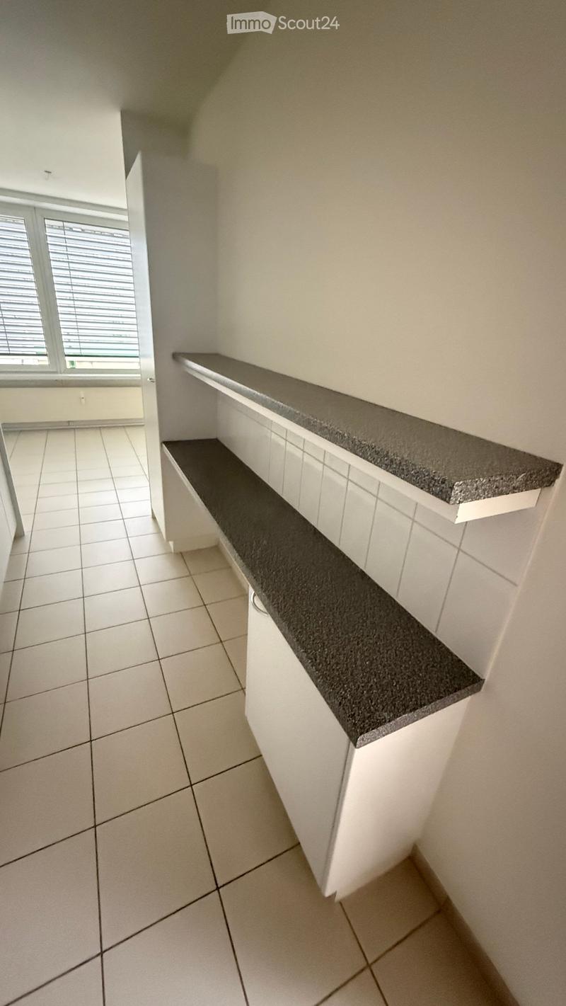 Empty room with white tiled floor, white walls, and a built-in shelf unit with a dark countertop.