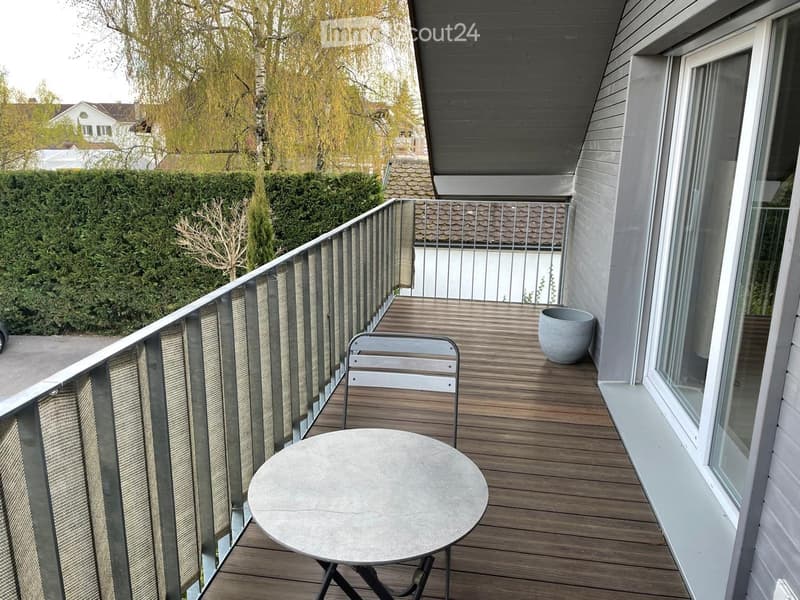 Balcony with wooden decking, metal railing, round table, chair, and decorative vase.