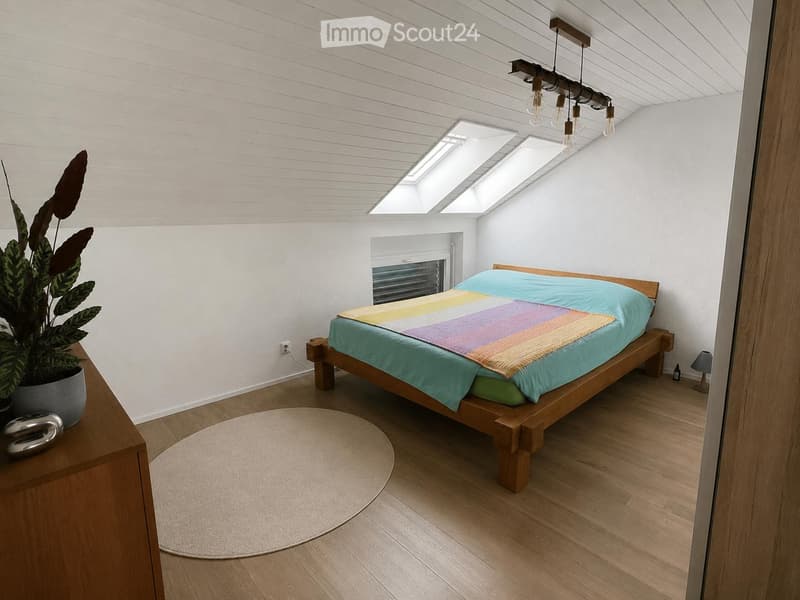 Modern bedroom with wooden bed, colorful striped duvet, round rug, potted plant, and pendant lighting.