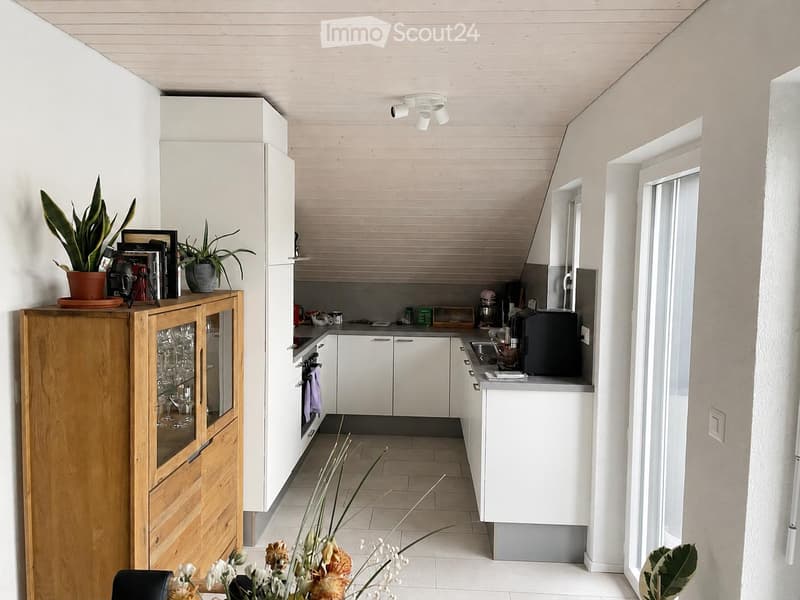 Modern kitchen with white cabinets, a wooden sideboard, and various appliances including a fridge, oven, and sink. The space features a tiled floor and a potted plant on the sideboard.