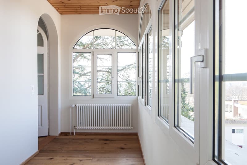 Empty hallway with wooden flooring, white walls, large windows, and a radiator. No furniture or equipment present.