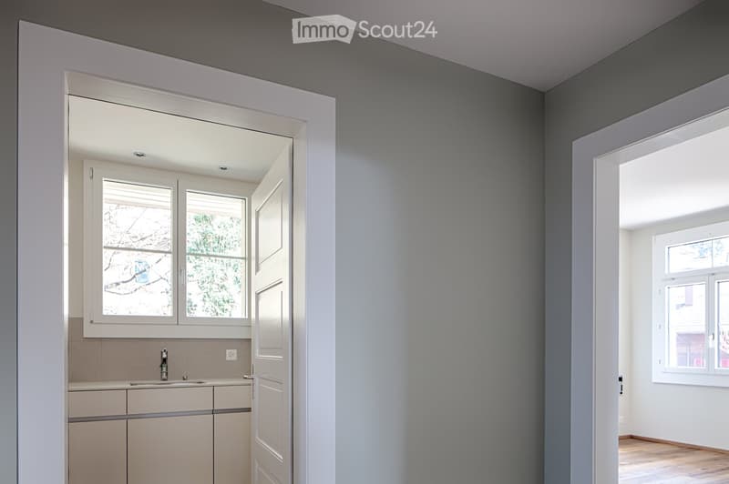 Empty room with grey walls, wooden floor, and large windows. No furniture or equipment present.