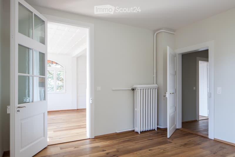 Bright, empty hallway with light wooden flooring, white walls, and multiple doors leading to other rooms.