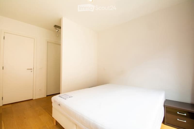 Minimalist bedroom with a single bed, nightstand, and wooden flooring.