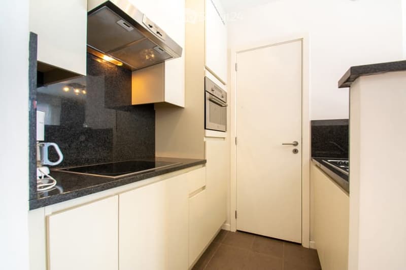 Modern kitchen with white cabinets, black countertops, and stainless steel appliances including a coffee maker, oven, and range hood.