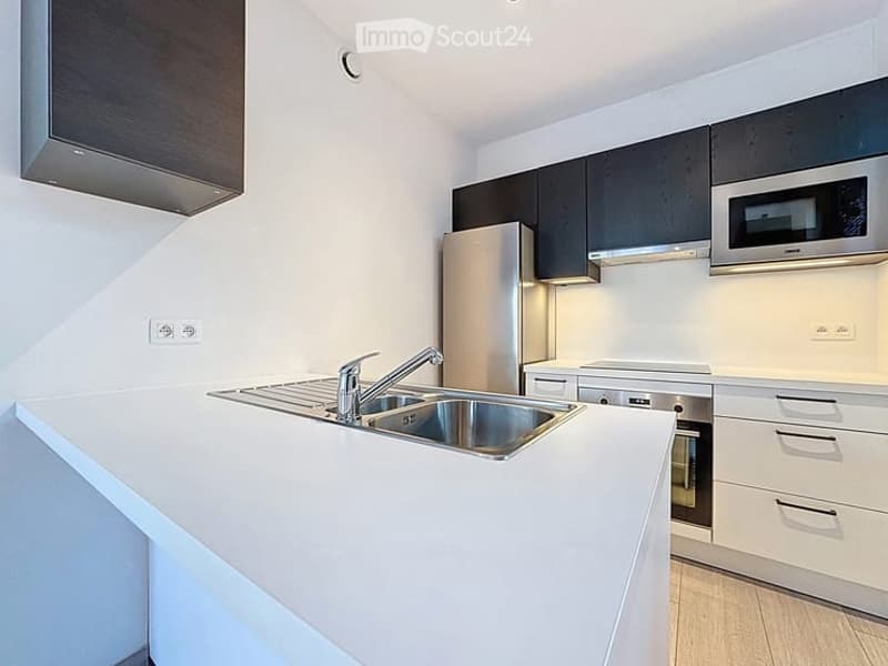 Modern kitchen with white countertops, stainless steel sink, and sleek black and white cabinetry.