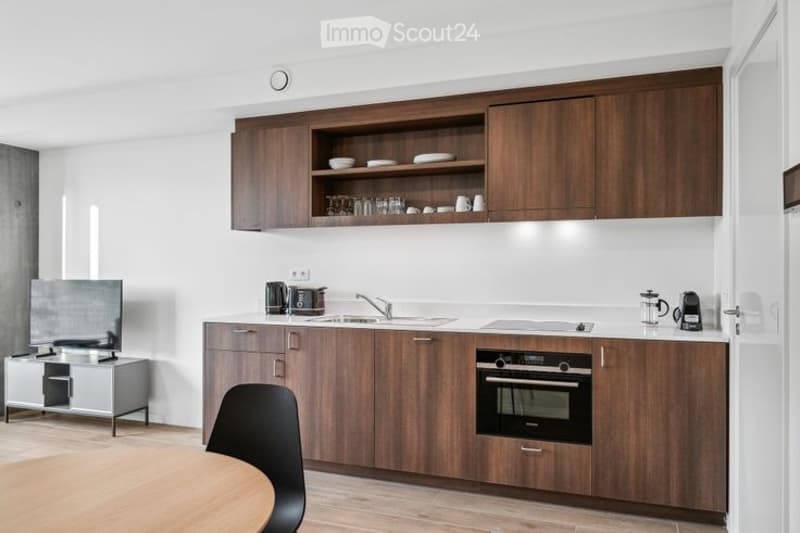Modern kitchen with wooden cabinets, stainless steel appliances, and a small dining area.