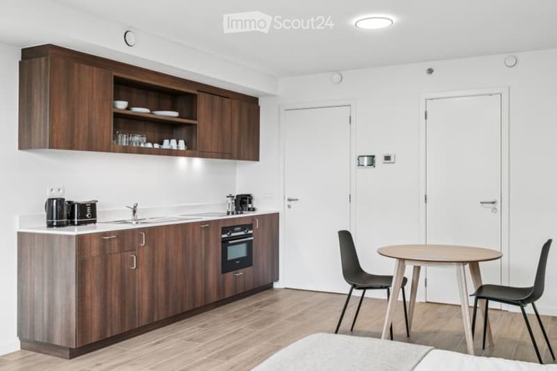 Modern, compact kitchen area with wooden cabinets, a sink, an oven, and a small dining table with chairs.