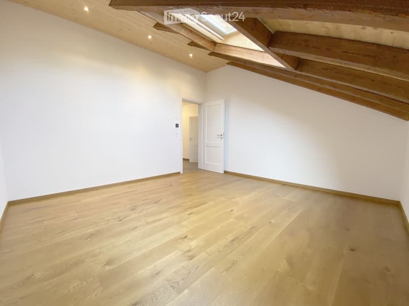 Empty room with wooden flooring, white walls, exposed wooden beams, and a skylight window in the ceiling.