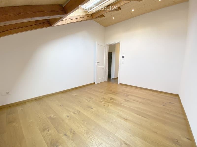 Empty room with wooden flooring, white walls, and a skylight in the ceiling. There are two open doors leading to other spaces.