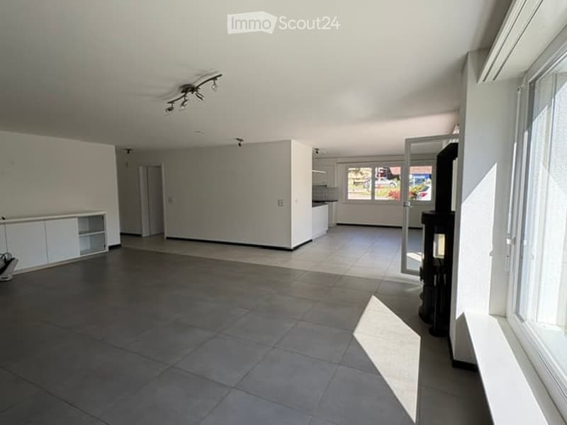Completely empty room with white walls, dark tiled floor, and large windows. No furniture or equipment.