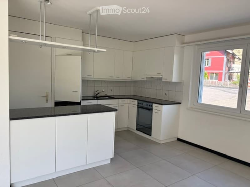 Modern kitchen with white cabinets, black countertops, and a built-in oven. Features a large window with a view of a red building outside.