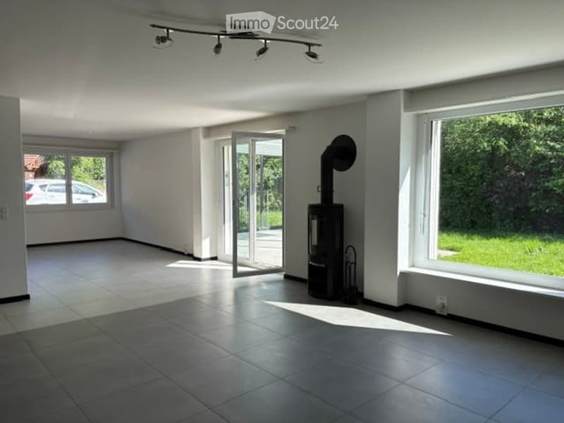 Empty room with white walls, tiled floor, large windows, and a sliding glass door leading to an outdoor area. No furniture or equipment is present.