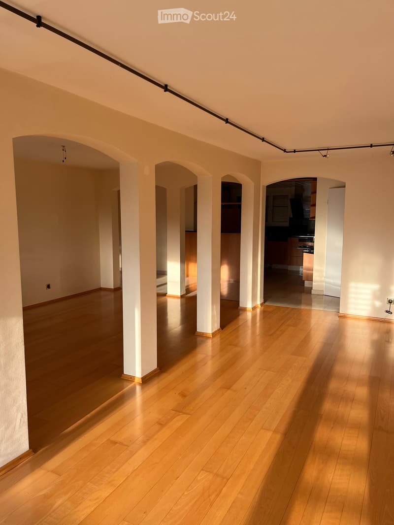 Empty room with polished wooden flooring, white walls, and several arched doorways leading to other rooms.